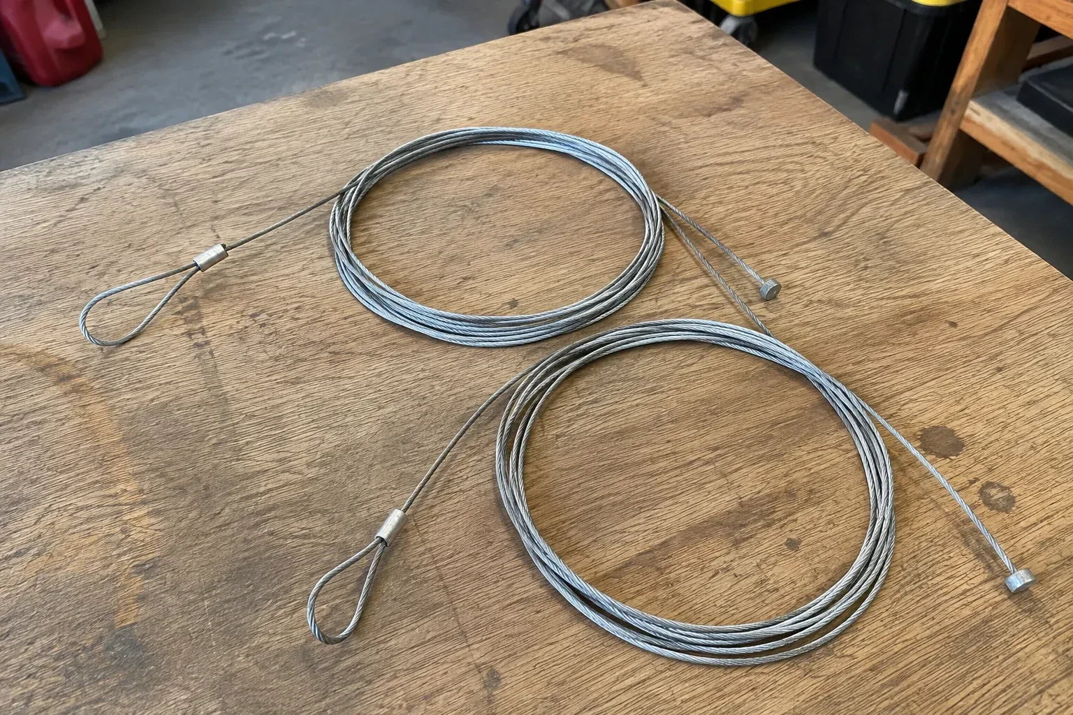 Two coiled steel cables with loop and stop ends on a workbench. — Garage Door Cable Replacement, Grimsby