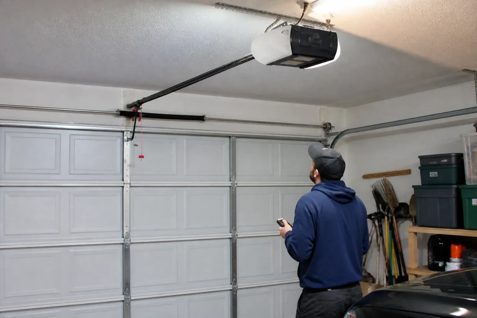 A person holding a remote looks toward an overhead garage-door opener and rail. — Garage Door Opener Diagnosis and Repair, Grimsby
