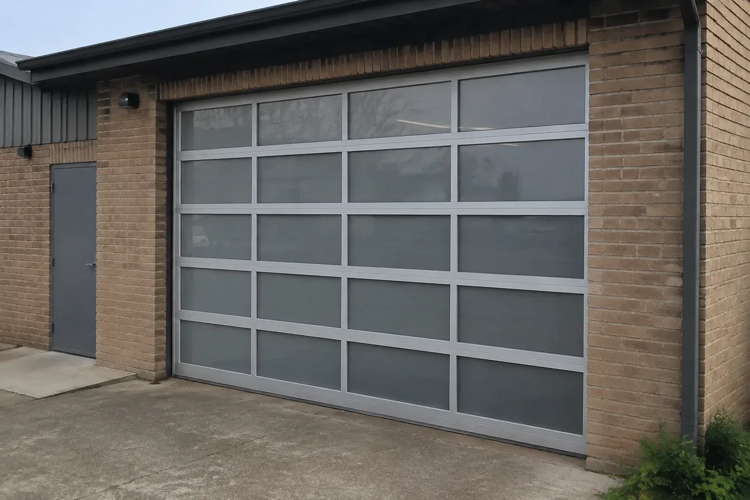 Closed glazed sectional door in a grey metal frame at a brick workshop. — Full-View Glass Garage Door Installation, Grimsby